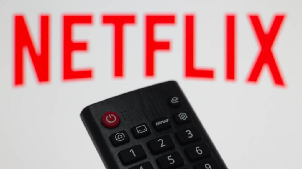 Acciones de Netflix: un control remoto de televisión frente al logo rojo de Netflix desenfocado al fondo