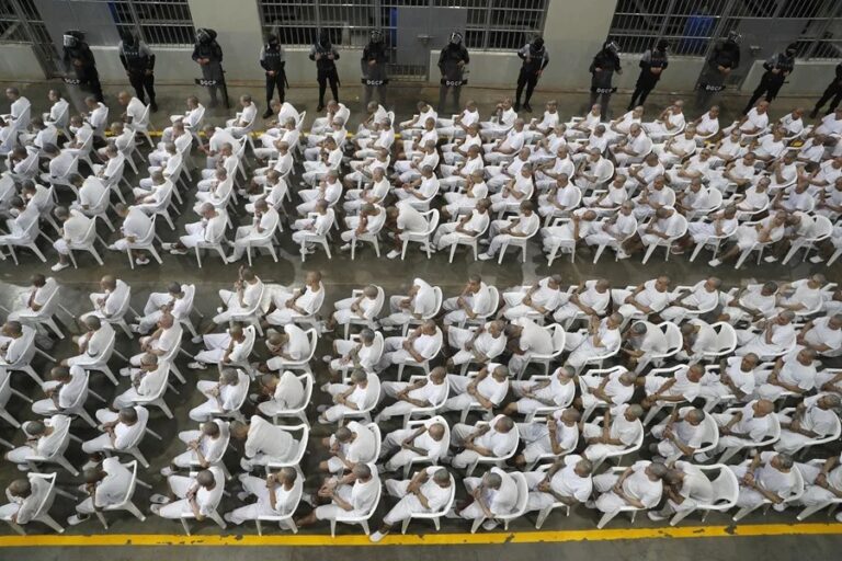 Cadena perpetua en El Salvador: decenas de reclusos vestidos de blanco sentados en filas dentro del CECOT bajo custodia de agentes