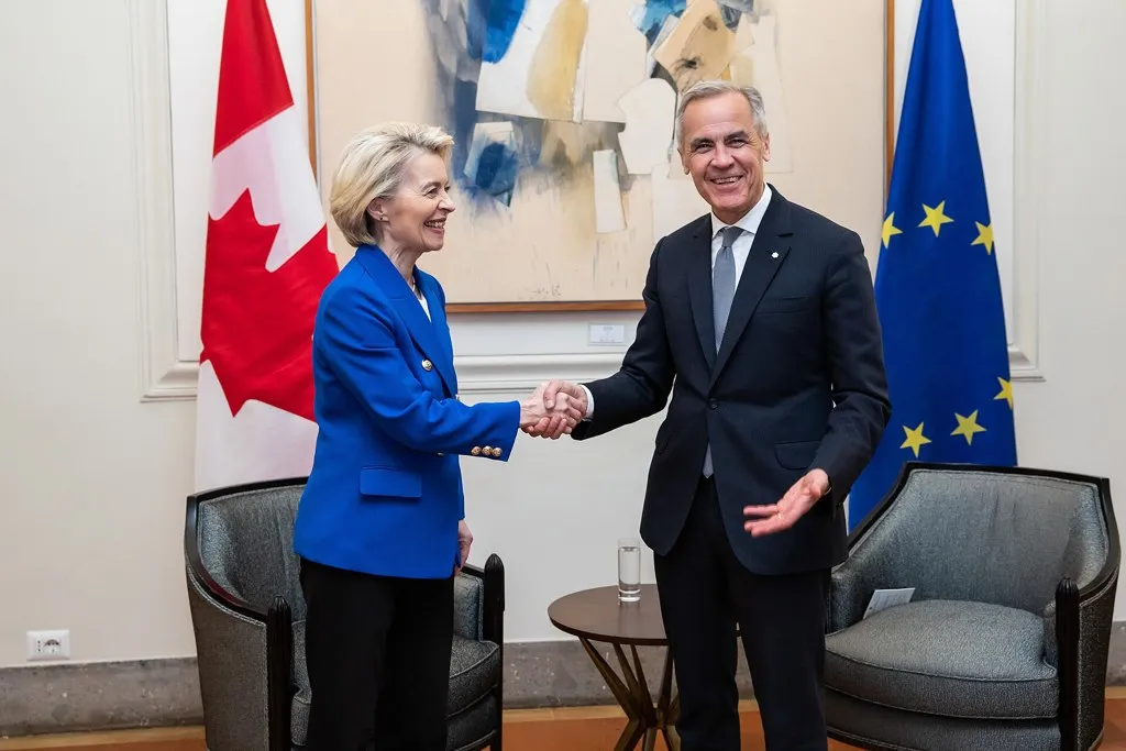 Ursula von der Leyen y Mark Carney se dan la mano entre las banderas de Canadá y la Unión Europea, en alusión a Canadá miembro asociado