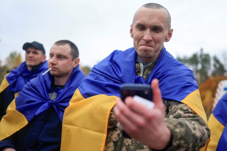 Prisionero ucraniano liberado en el canje de prisioneros Ucrania y Rusia habla por teléfono envuelto en la bandera de Ucrania
