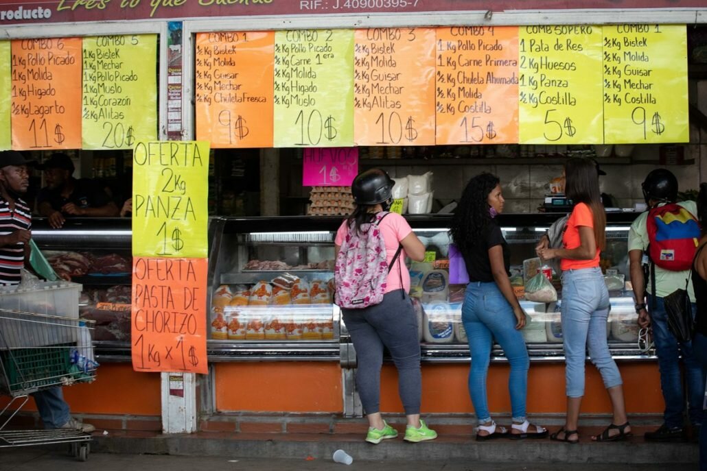 Compradoras frente a un puesto de carnes con precios en dólares en un mercado venezolano, en medio de la inflación en Venezuela