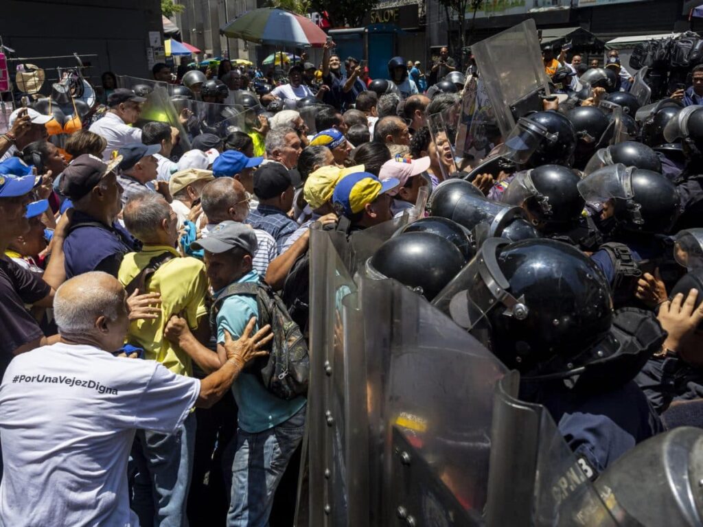 Manifestantes y jubilados frente a un cordón de policías antimotines durante una protesta en Venezuela, en el contexto de las detenciones políticas en Venezuela