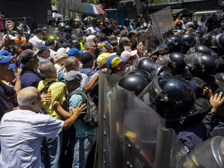 Manifestantes y jubilados frente a un cordón de policías antimotines durante una protesta en Venezuela, en el contexto de las detenciones políticas en Venezuela