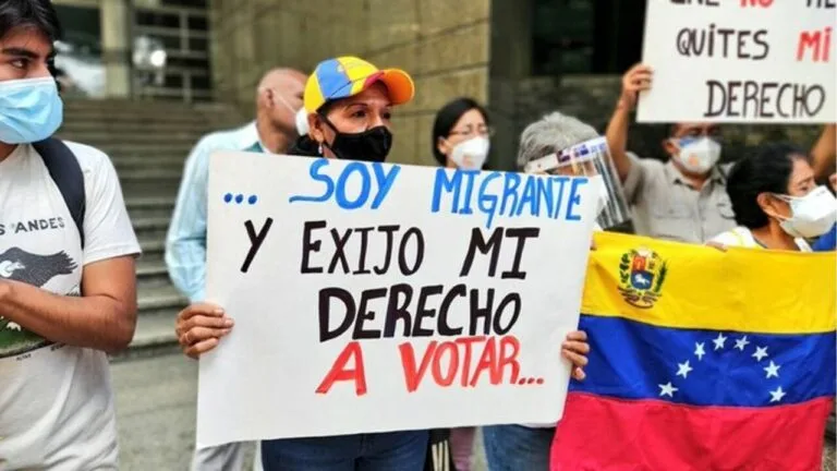 Una migrante de la diáspora venezolana sostiene un cartel que exige su derecho a votar, junto a la bandera de Venezuela
