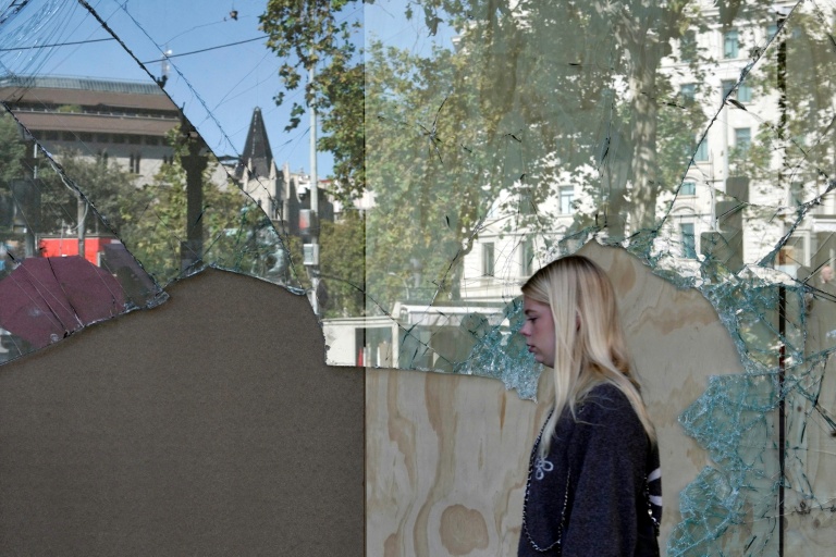 Disturbios en Barcelona: una mujer pasa ante un escaparate destrozado en el centro de la ciudad tras la noche de disturbios