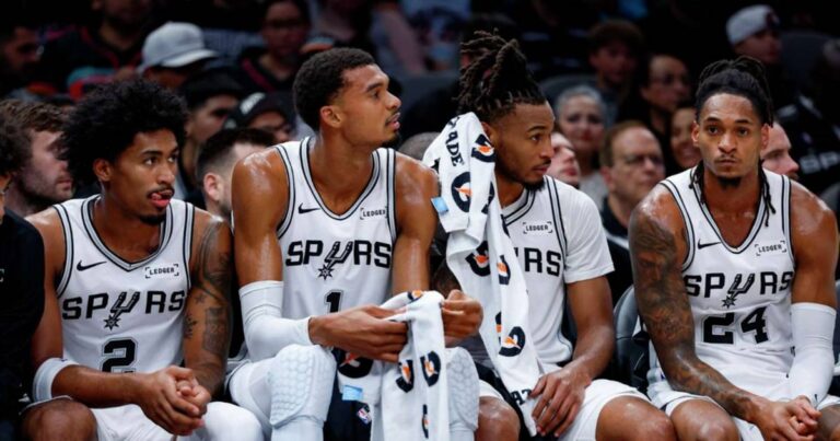 Dylan Harper titular con el uniforme número 2 de los Spurs, sentado junto a Victor Wembanyama en la banca de San Antonio