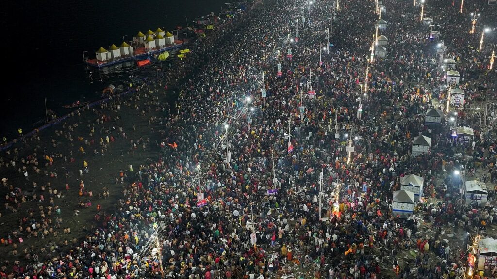 Vista aérea nocturna de una multitud masiva junto al agua durante un festival religioso en India: estampida en India