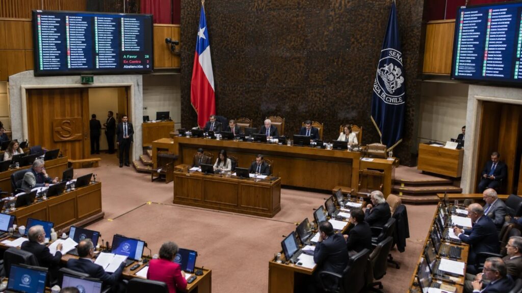 Sala del Senado de Chile durante la votación de la ley de expulsión de migrantes en Chile, con la bandera chilena y el tablero de votación