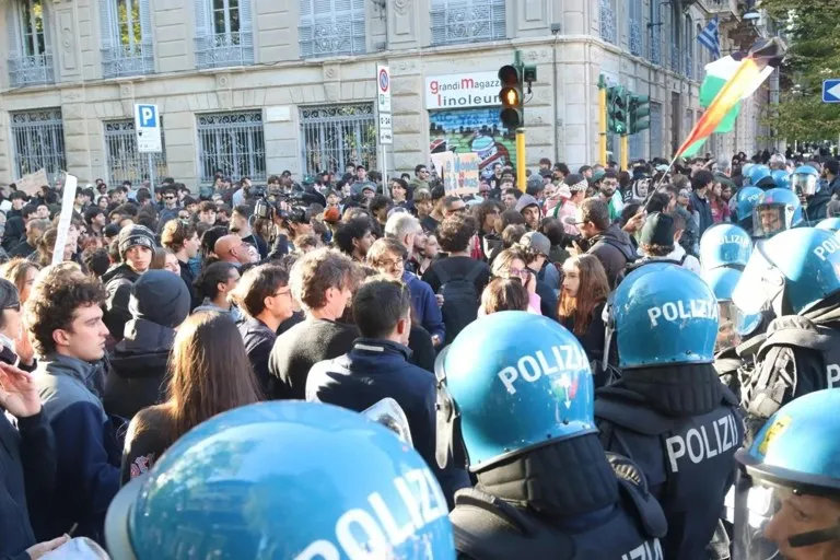 huelga general en Italia: multitud de jóvenes manifestantes frente a un cordón de policías con cascos en una calle italiana durante las protestas de este viernes