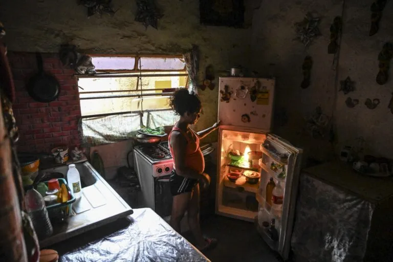 Inseguridad alimentaria en Venezuela: una mujer embarazada abre una nevera casi vacía en la cocina de su casa