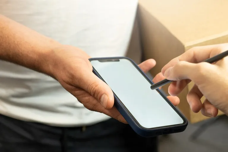 Comprador firmando en su celular la entrega de un paquete de una compra en línea, por el IVA a compras en Temu y Shein del 19 %