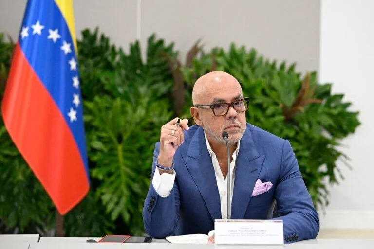 Jorge Rodríguez habla de los recursos del petróleo: el presidente de la Asamblea Nacional, sentado en una mesa con micrófono junto a la bandera de Venezuela