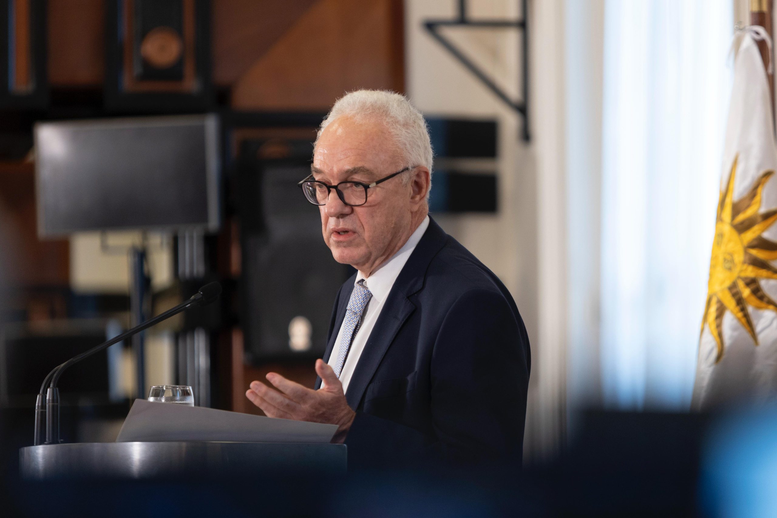Uruguay descarta reanudar relaciones con Venezuela: el canciller Mario Lubetkin en un atril con la bandera uruguaya
