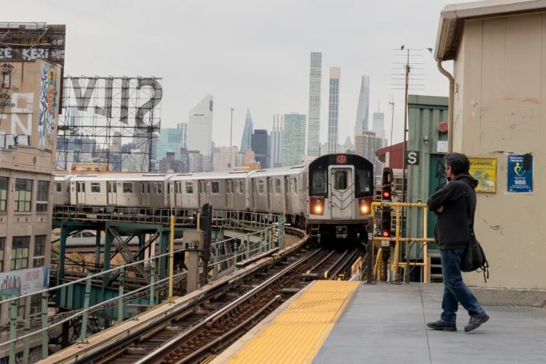 Un tren del Metro de Nueva York llega a una estación elevada de Queens con Manhattan al fondo