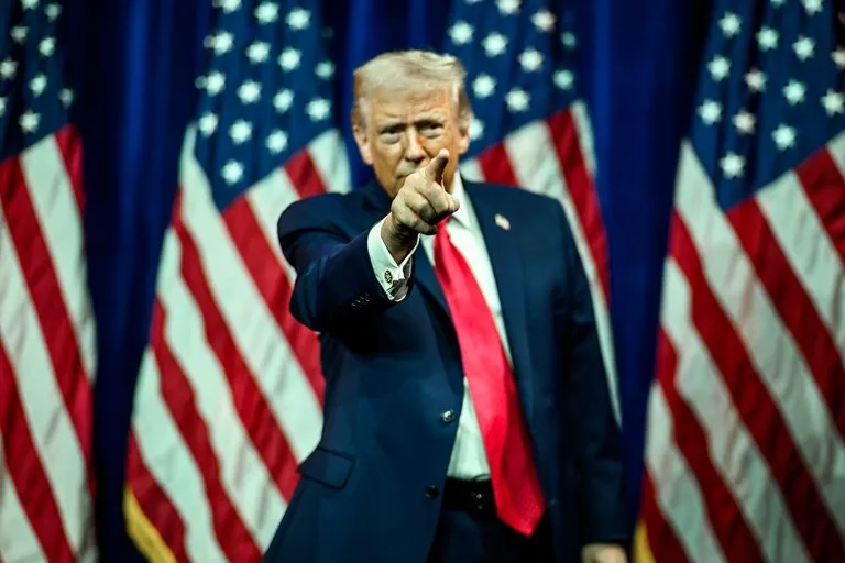 Donald Trump señala a la cámara durante un acto con banderas de Estados Unidos, en una foto oficial previa a la reanudación de los mítines de Trump en Iowa y Kansas