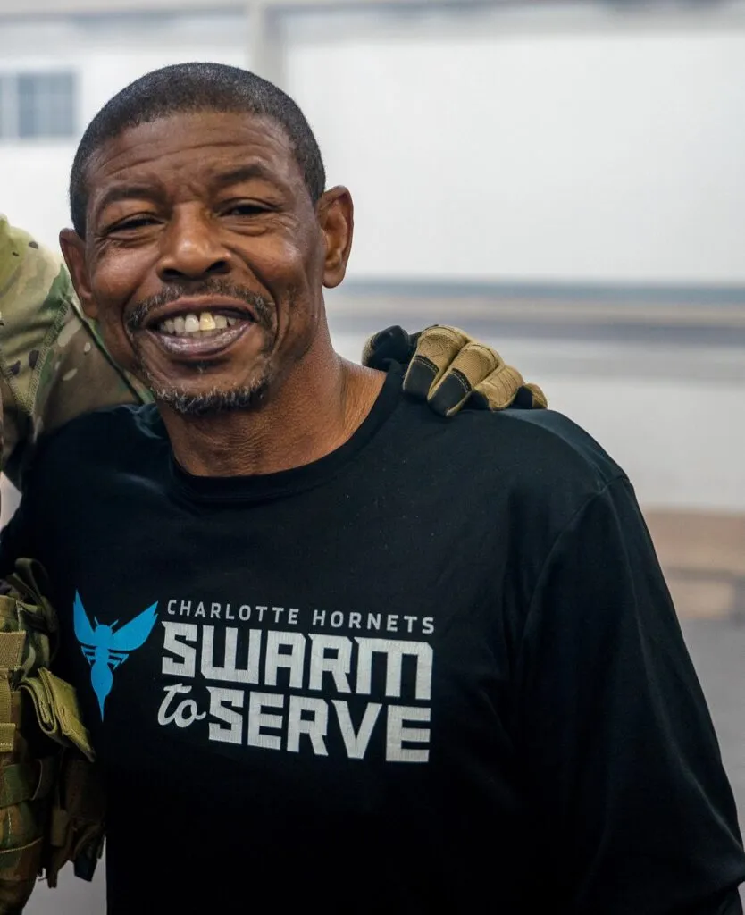 Muggsy Bogues sonríe con una camiseta de los Charlotte Hornets durante un acto comunitario