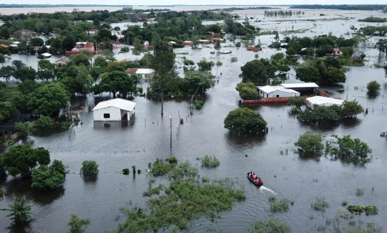 El Nino en America Latina: vista aerea de una comunidad inundada en Sudamerica, con casas rodeadas de agua y vecinos en una lancha