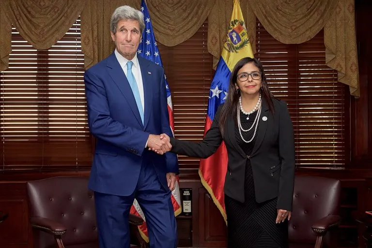 Delcy Rodríguez, entonces canciller de Venezuela, estrecha la mano del secretario de Estado de EE. UU., John Kerry, ante las banderas de ambos países
