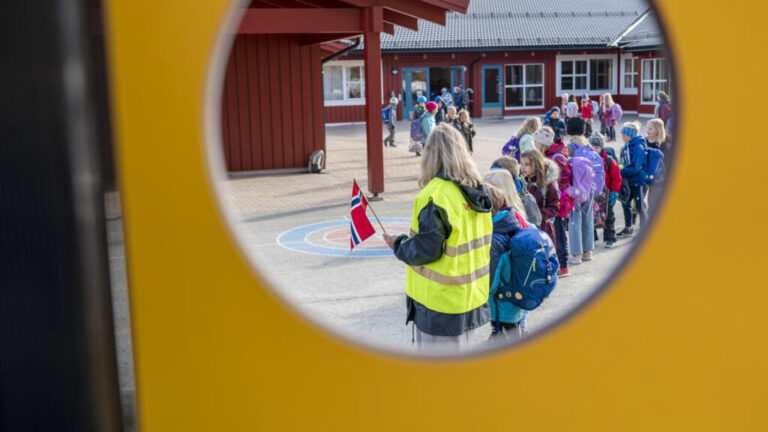 Plataformas dañinas a menores en Noruega: niños con mochilas a la salida de una escuela noruega, junto a una maestra con un chaleco reflectante y una bandera del país