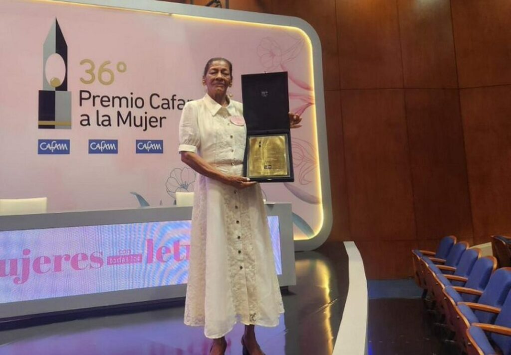 Premio Cafam a la Mujer: una ganadora de una edición anterior sostiene su placa de reconocimiento en el escenario del galardón