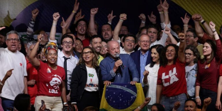 Primer discurso de Lula tras ganar en Brasil: Lula habla con un micrófono sosteniendo la bandera de Brasil, rodeado de su equipo y seguidores que celebran en São Paulo