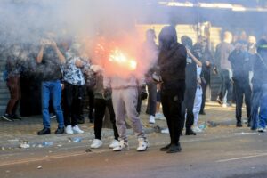 Protestas en Albania: un manifestante encapuchado sostiene una bengala encendida entre el humo en una calle de Tirana
