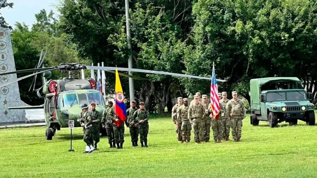Soldados estadounidenses en Colombia: formacion conjunta de militares de Colombia y Estados Unidos con las banderas de ambos paises, un helicoptero y un vehiculo militar en Tolemaida