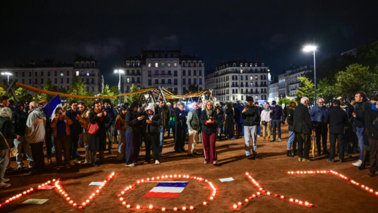 Concentración nocturna en Lyon durante los toques de queda en Francia, con velas y una bandera francesa