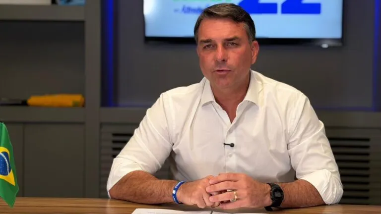 Flávio Bolsonaro, investigado por la posible financiación extranjera de su campaña, sentado a un escritorio junto a una bandera de Brasil