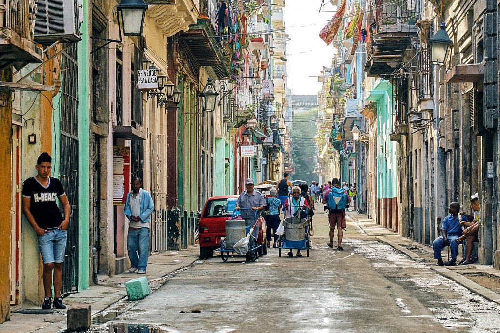 Turismo internacional en Cuba: calle de La Habana con vecinos y un visitante con mochila