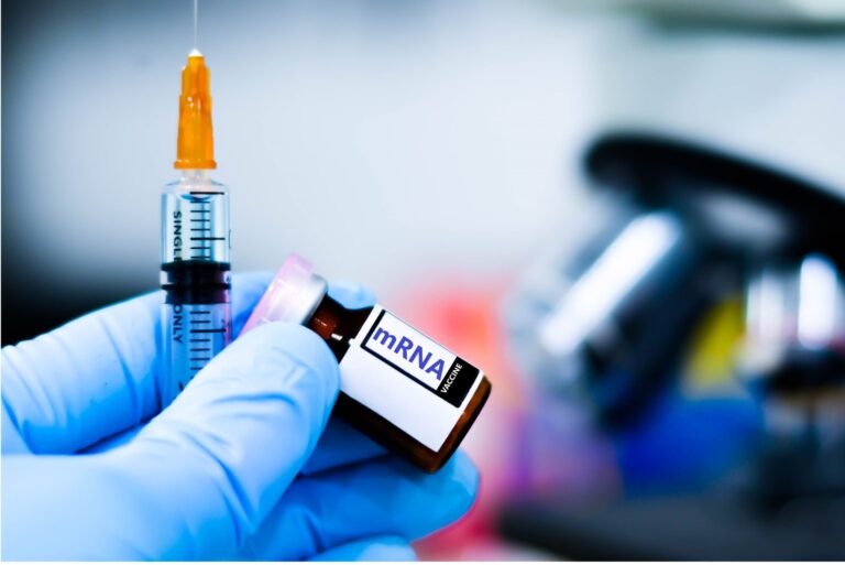 Vial de una vacuna de ARNm contra el melanoma junto a una jeringa, sostenido por una mano con guante en un laboratorio
