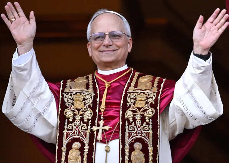 Viaje del papa León XIV: el pontífice saluda con ambas manos levantadas con su estola roja y dorada