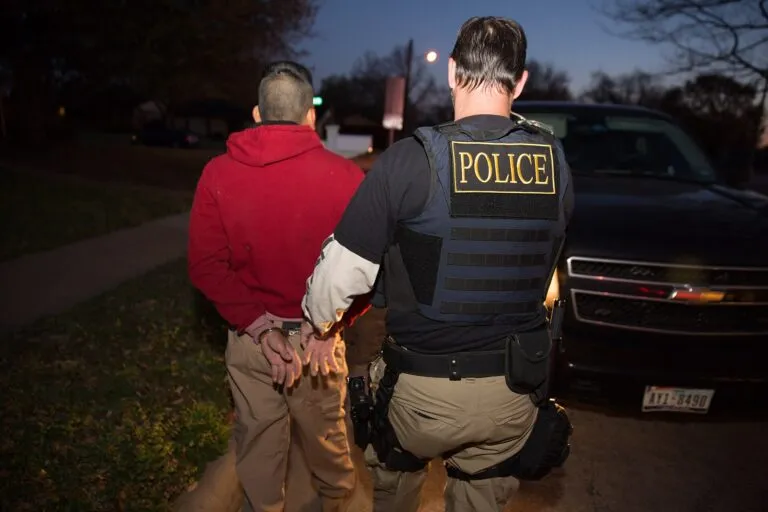 Un oficial de ICE ERO escolta a un hombre esposado durante un operativo en Estados Unidos; dos extranjeros fueron acusados de voto ilegal en Nevada