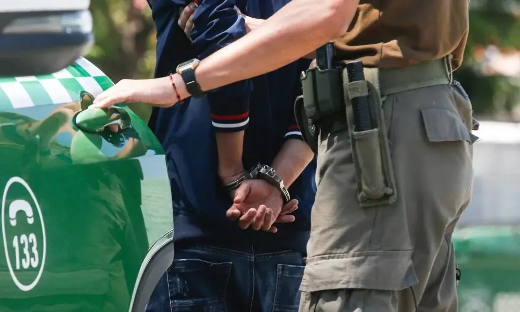 Un funcionario de Carabineros custodia a un detenido junto a un vehículo policial en Chile, en una imagen referencial del caso de la zuliana en Chile